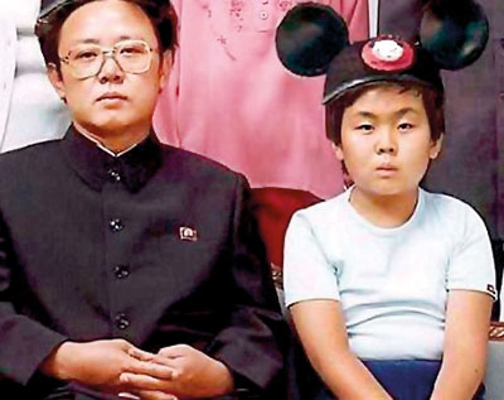 Rare picture of a young Kim Jong-un with father and former North Korea leader Kim Jong-il. The future leader enduring a punishment at a young age, being compelled to wear the daily fashion attire of the corrupted enemy to the east.